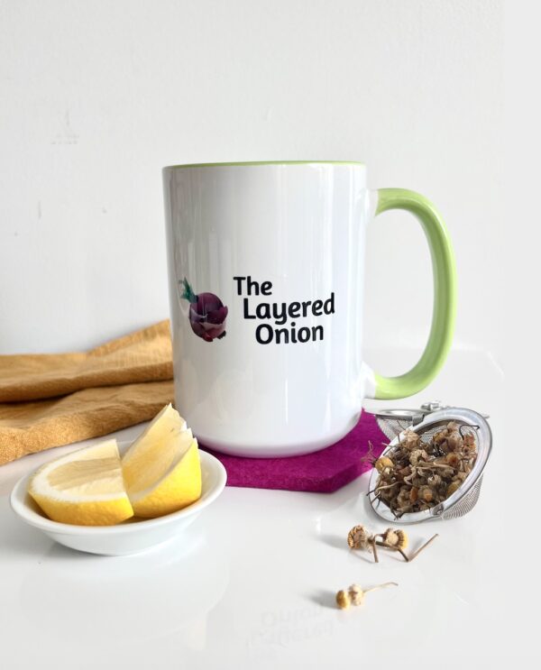 TLO mug with green handle, loose leaf chamomile tea on the right, and lemon wedges on the left.