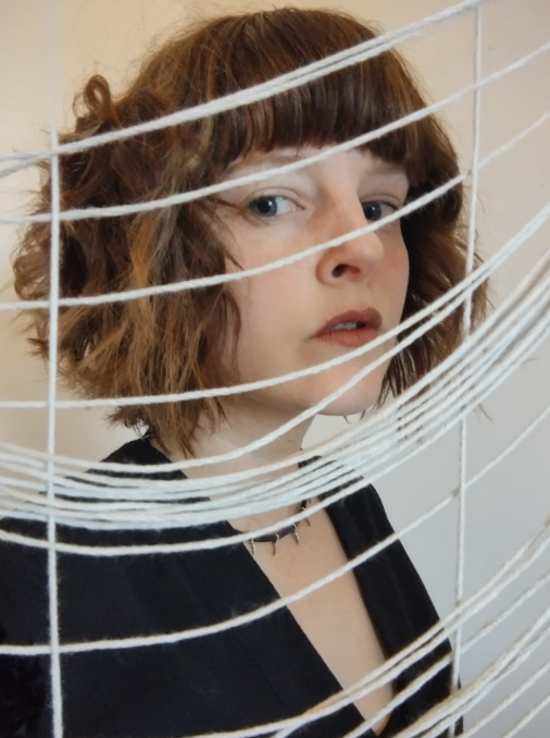 A photo of the artist, Lauren E. Allen, behind string. The artist works with photography and vintage cameras. 

She uses art to heal and process. Neurodivergent. Neurodivergence. Art to address mental health - art for mental health.