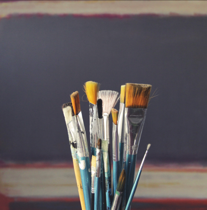 Serene image of clean paint brushes on an indigo background with a white stripe at the bottom. The brushes are of various sizes.