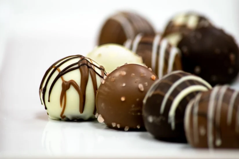 A photo of small caramel truffles in white, milk, and dark chocolate.
